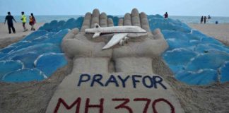 Beachgoers walk past a sand sculpture made by Indian sand artist Sudersan Pattnaik with a message of prayers for the missing Malaysian Airlines Flight MH370 at Puri beach in India March 12, 2014