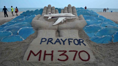 Beachgoers walk past a sand sculpture made by Indian sand artist Sudersan Pattnaik with a message of prayers for the missing Malaysian Airlines Flight MH370 at Puri beach in India March 12, 2014