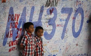 Two Malaysian children stand in front of messages board and well wishes to people involved with the missing Malaysia Airlines jetliner MH370, Sunday, March 16, 2014
