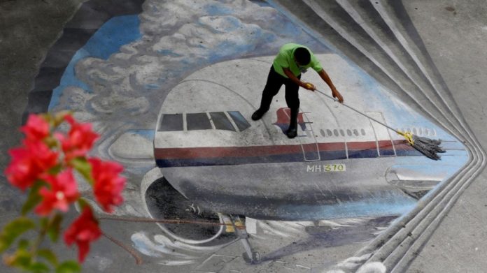 A school utility worker mops a mural depicting the missing Malaysia Airlines Flight 370 Tuesday,