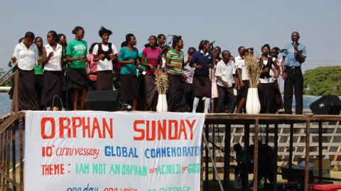 In this 2012 photo provided by the Christian Alliance for Orphans, a pastor, right, speaks on stage accompanied by orphaned children from the Lusaka region