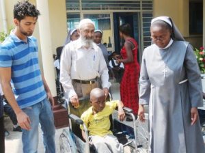 Italian Hospital Acting Administrator Sr. Ireen Kunda  and Donations Coordinator Haroon Ghumra placing   Sylvester Chali,6 years old and Livingstone resident,  in his newly donate wheel chair while looking on is Cardinal Distributors MD Safwaan Patel.