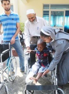 Italian Hospital Acting Administrator Sr. Ireen Kunda  placing   Philip Kusa, 4 years old and Chipata resident,  in his newly donate wheel chair while looking on are Cardinal Distributors MD Safwaan Patel and Donations Coordinator Haroon Ghumra.