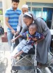Italian Hospital Acting Administrator Sr. Ireen Kunda  placing   Philip Kusa, 4 years old and Chipata resident,  in his newly donate wheel chair while looking on are Cardinal Distributors MD Safwaan Patel and Donations Coordinator Haroon Ghumra.