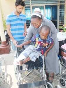 Italian Hospital Acting Administrator Sr. Ireen Kunda  placing   Philip Kusa, 4 years old and Chipata resident,  in his newly donate wheel chair while looking on is Cardinal Distributors MD Safwaan Patel..
