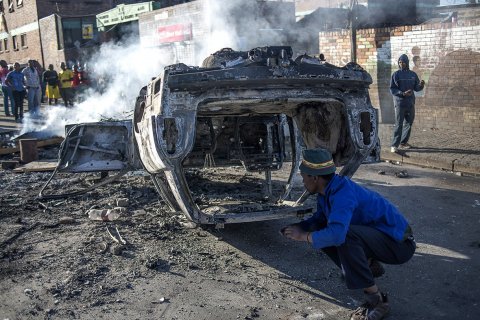 People look at a burnt-out car after foreign nationals reportedly torched it in the early hours outside a hostel in the Jeppestown area, east of Johannesburg(Mujahid Safodien:AFP) People look at a burnt-out car after foreign nationals reportedly torched it in the early hours outside a hostel in the Jeppestown area, east of Johannesburg(Mujahid Safodien:AFP)