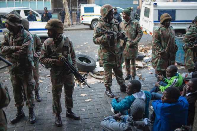 South African police and soldiers guard migrants after raiding buildings in Johannesburg's central business district on May 8, 2015 in an operation where over 300 illegal immigrants and foreign nationals were arrested (AFP Photo/Mujahid Safodien)